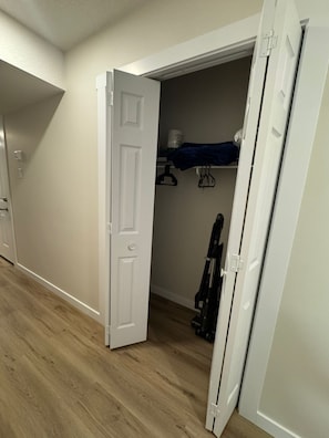 Een kamer met een houten vloer, een witte deur en een kast met hangende kleding.