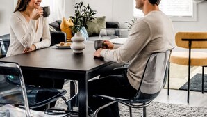 Un espace de salle à manger moderne avec une table ronde, des chaises transparentes, un luminaire suspendu et une grande fenêtre ornée de rideaux légers.