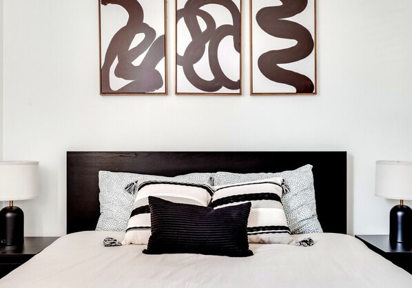 A neatly made bed with a black headboard, white bedding, and striped pillows. - 3BR Ottawa | Parking | Monthly Stays (Ottawa)
