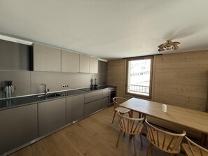 A modern kitchen with grey cabinets, a wooden dining table, and two chairs. - 10m from ski slopes, fitness, swimming pool, sauna, hammam, balcony, tv, ski locker, 104m² (Huez)