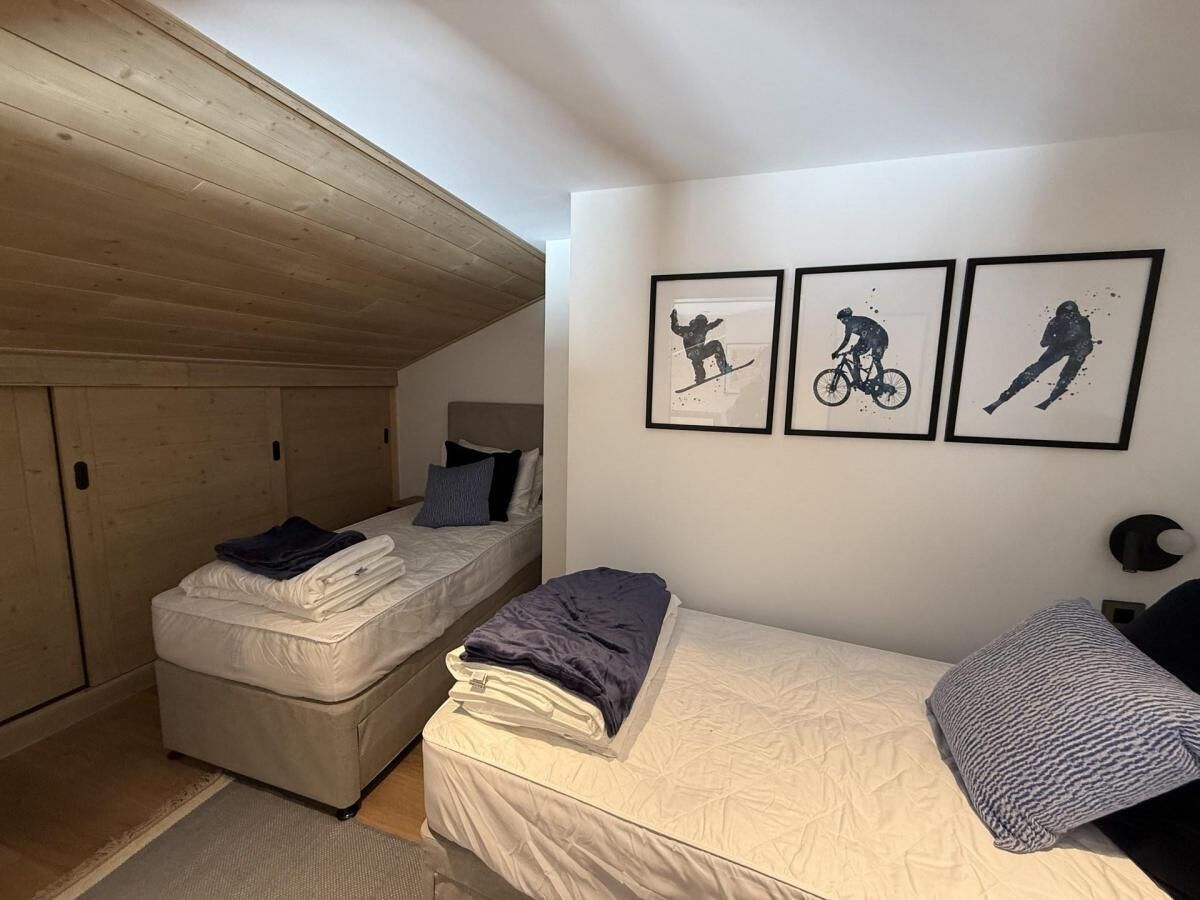 A bedroom with two beds, a wooden ceiling, and three framed pictures on the wall.