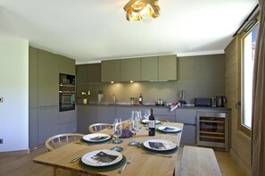 A modern kitchen with built-in appliances, a dining table set for four, and a large window providing natural light. - 10m from ski slopes, fitness, swimming pool, sauna, hammam, balcony, tv, ski locker, 104m² (Huez)