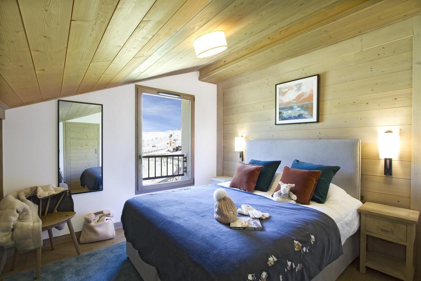 A bedroom with a bed, bedside lamps, a window with a view, a mirror, and a wooden ceiling.