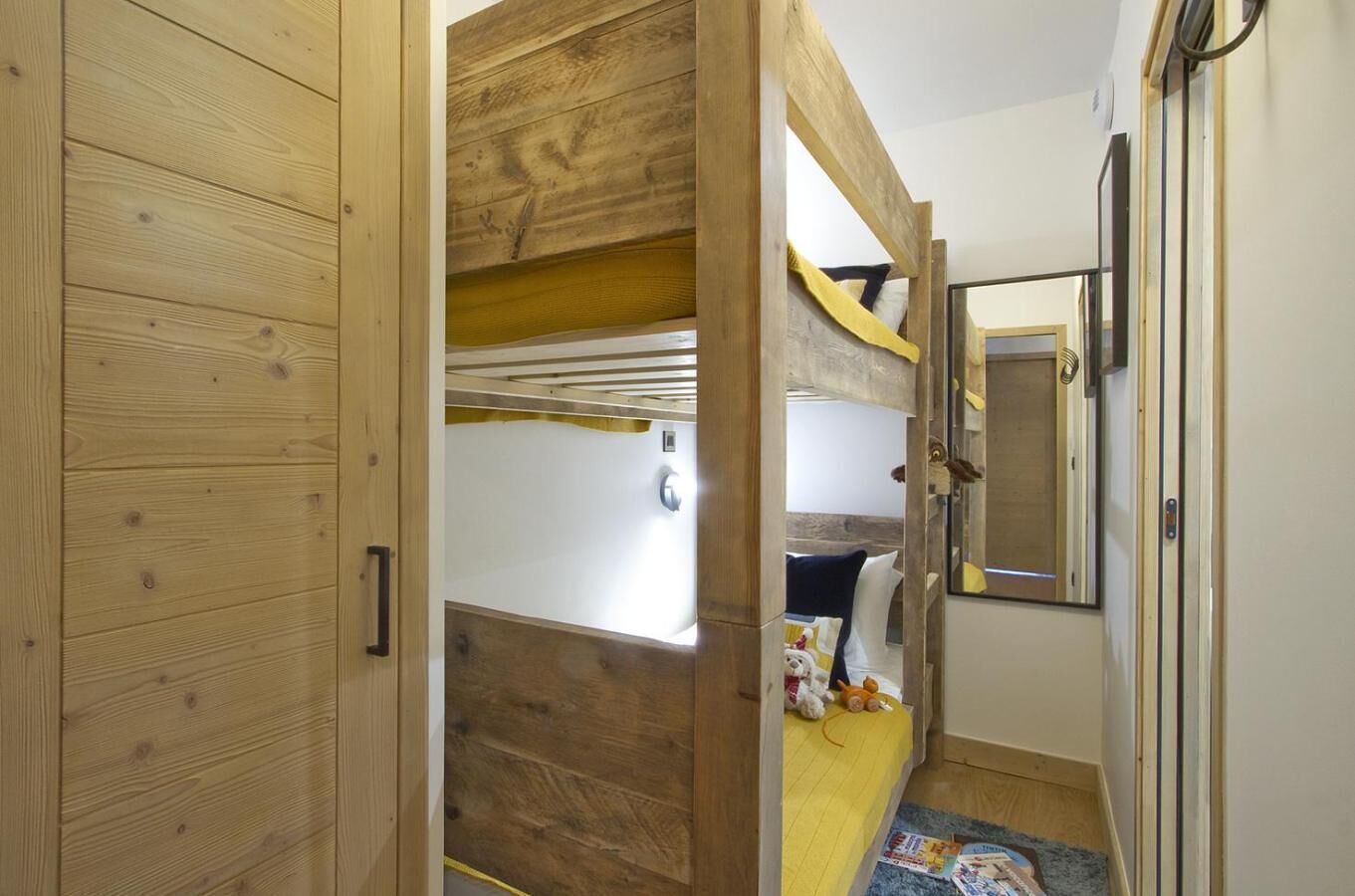 Ein Zimmer mit einem Etagenbett, einer Holztür, einem Spiegel und einem kleinen Tisch mit Gegenständen darauf.