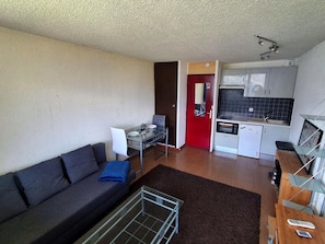 A compact living space with a sofa, a small dining table, a kitchenette, and a red door. - 200m from ski slopes, 7th floor, tv, 24m², Tignes (Tignes)
