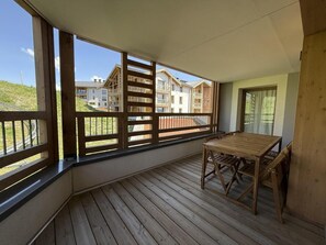 Eine Holzterrasse mit Tisch und Stühlen, großen Fenstern und Blick auf Gebäude.