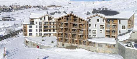 A multi-story hotel with a wooden facade, large windows, and a ski slope in the background.