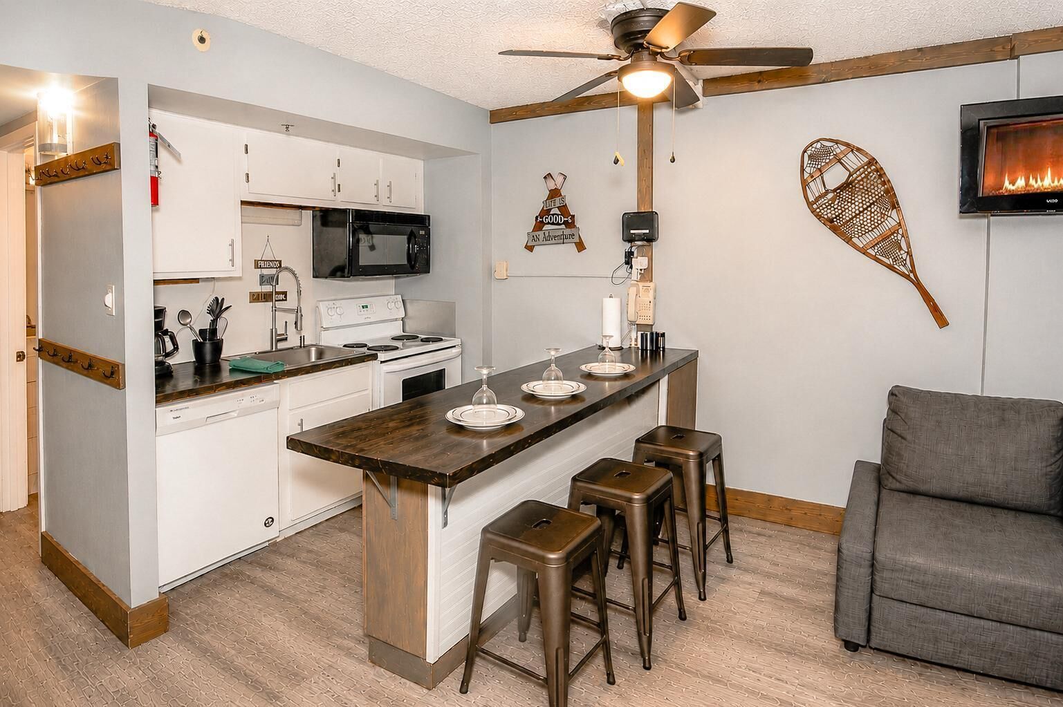 A compact kitchen with a central island, a ceiling fan, and a flat-screen TV mounted on the wall.