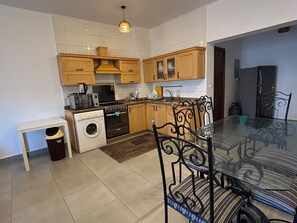 A kitchen with wooden cabinets, a washing machine, a stove, and a dining table with chairs. - Amwaj - 3bedroom chalet (Marsa Matrouh Governorate)