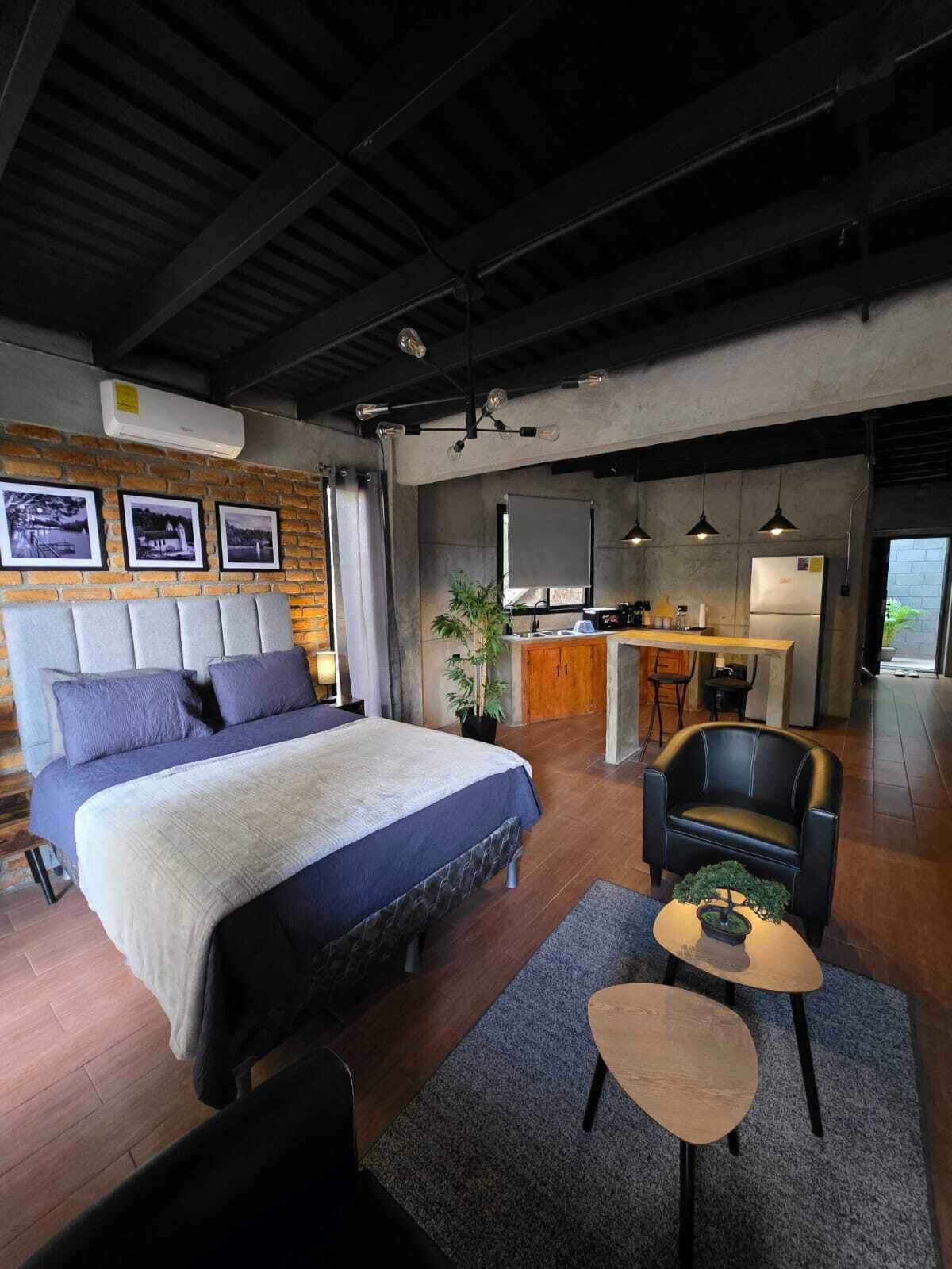 Una habitación de hotel moderna con una cama grande, una zona de estar, una kitchenette y vistas al exterior.