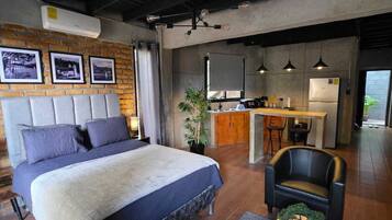 Una habitación de hotel moderna con una cama grande, una zona de estar, una kitchenette y vistas al exterior.