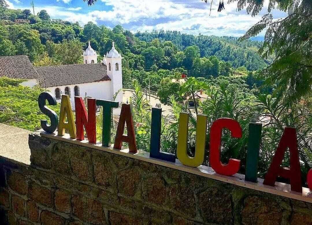 A stone wall with colorful letters spelling 'SANTA LUCIA' and a white building with a dome in the background.