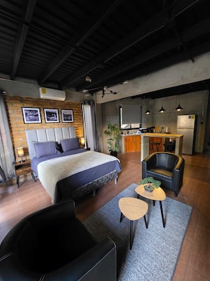A modern hotel room with a large bed, a desk, a chair, and a small table.