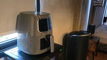 Una cafetera sobre una encimera con una toalla y un recipiente negro, probablemente para posos de café, en una habitación con una ventana y una puerta al fondo.