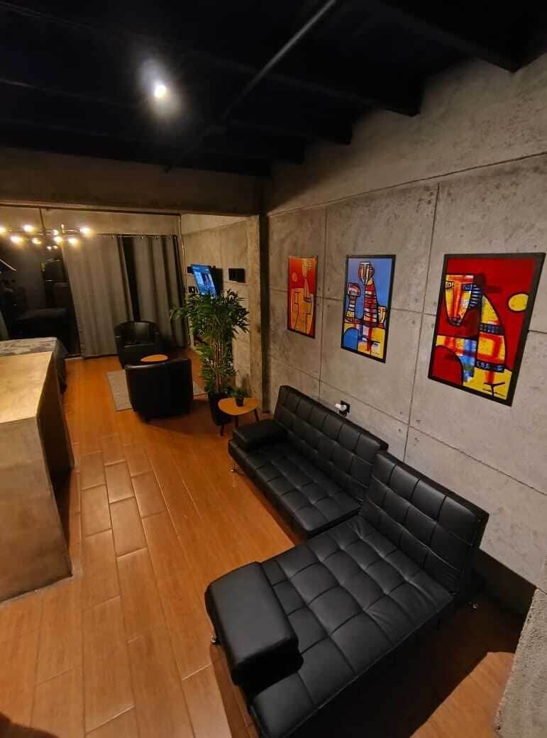 A modern living room with a black leather sofa, wooden flooring, and abstract art on the walls.