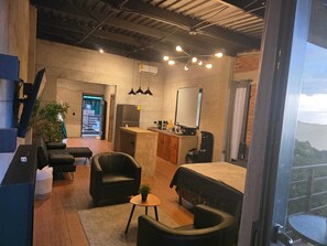 Habitación de hotel compacta con cama, un pequeño rincón de descanso, kitchenette y un ventanal con vistas al exterior.