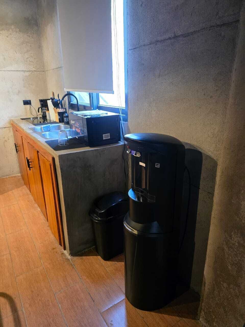 Ett kompakt kök med en kaffebryggare, en papperskorg och ett fönster som släpper in naturligt ljus.