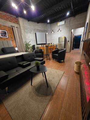 Un área de estar moderna con un sofá, sillas, una mesita con una planta y una zona de bar con taburetes.