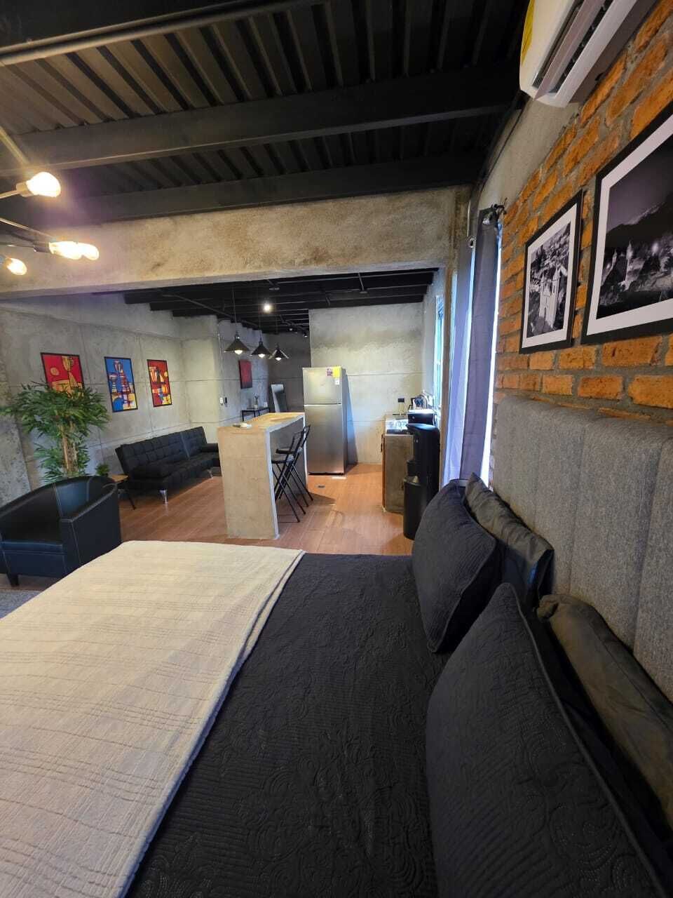 Una stanza moderna con un letto, un divano, un angolo cottura e una parete in mattoni decorata con immagini.