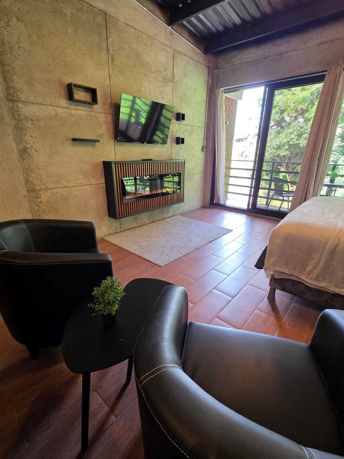A modern room with a sofa, a small table with a plant, a TV mounted on the wall, and a bed with a view of the outdoors.