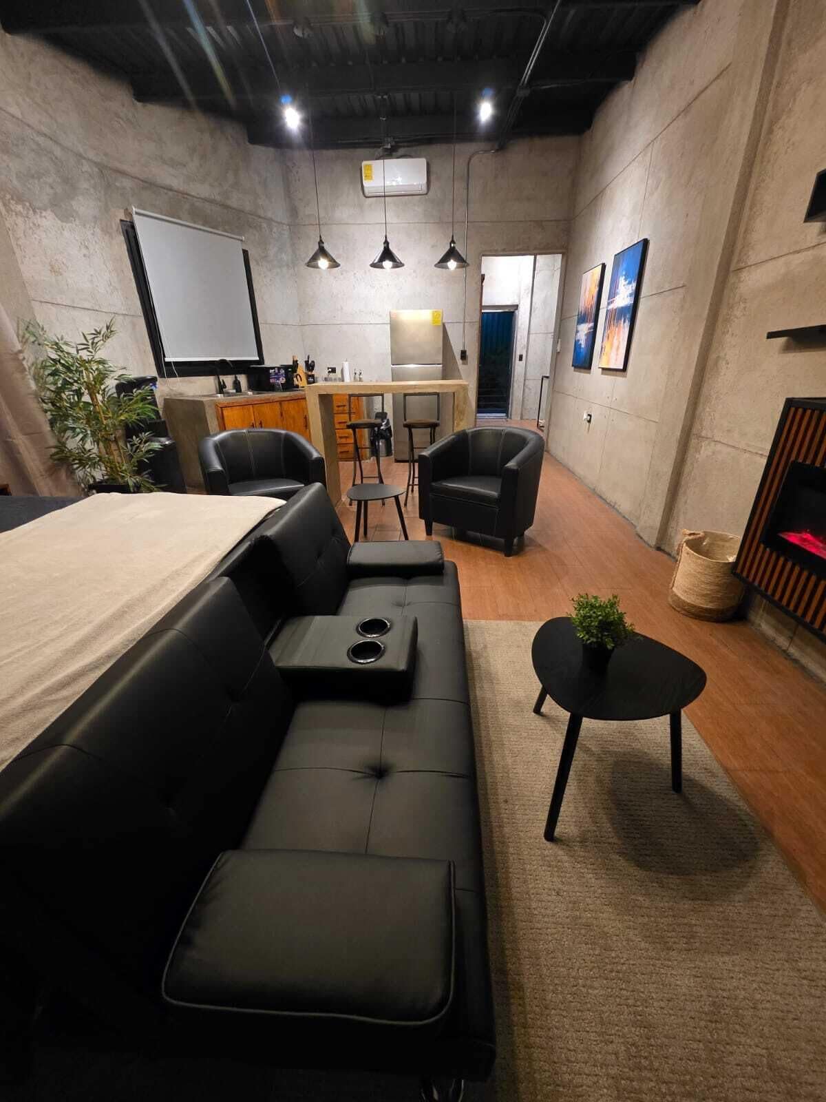 A modern interior with a sofa, chairs, a small table, a kitchen area, and artwork on the walls.