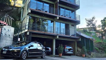 Um edifício com várias andares, varandas, área de estacionamento e um carro estacionado na frente.