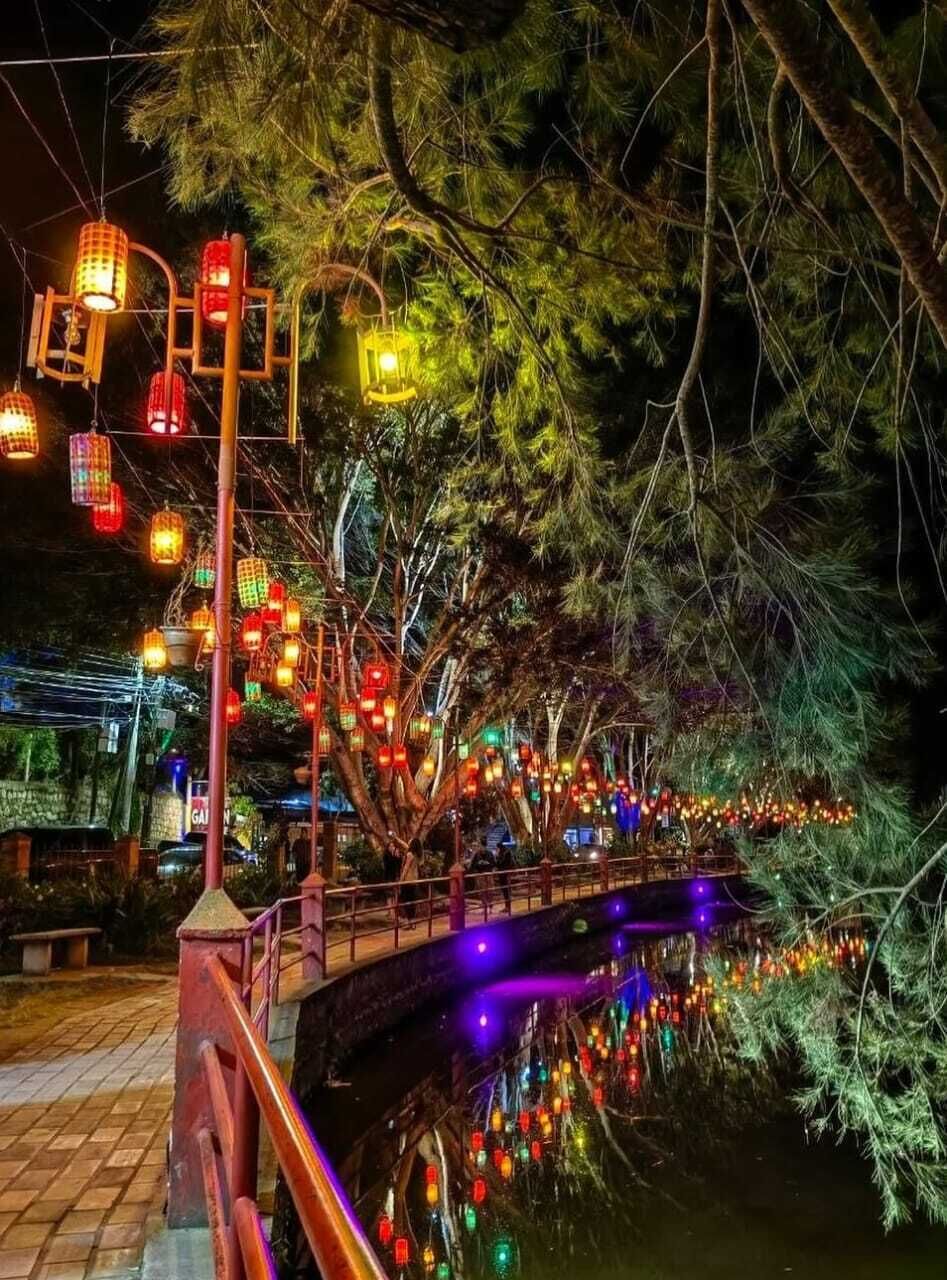 A bridge with colorful lanterns and lights, surrounded by trees.