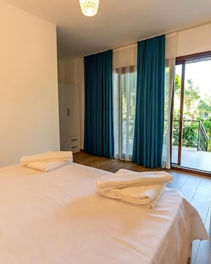 A hotel room with a bed, a wardrobe, a balcony with curtains, and a view of greenery. - Doğa pansiyon (Marmaris)
