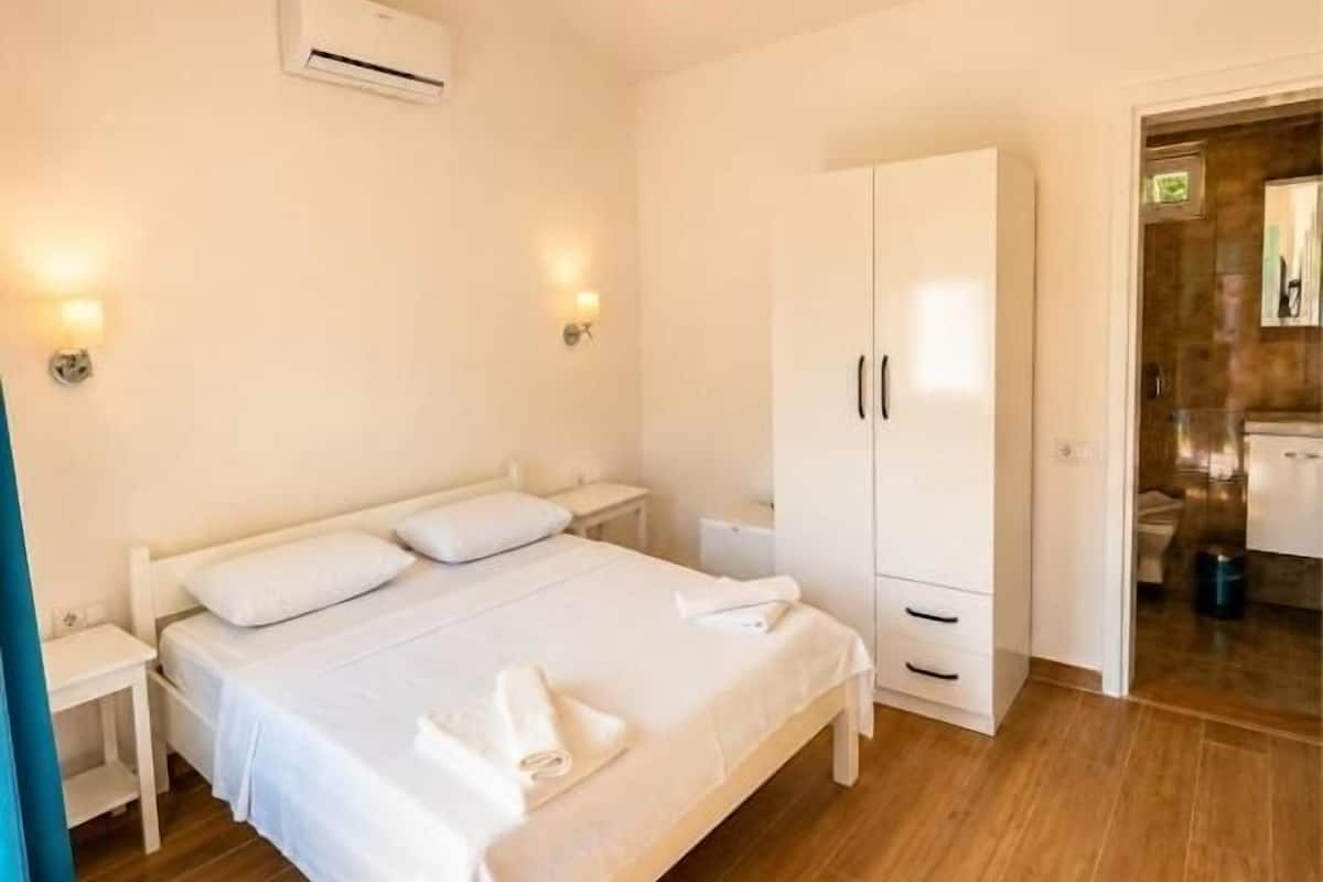 A bedroom with a bed, bedside tables, a wardrobe, and an air conditioning unit.