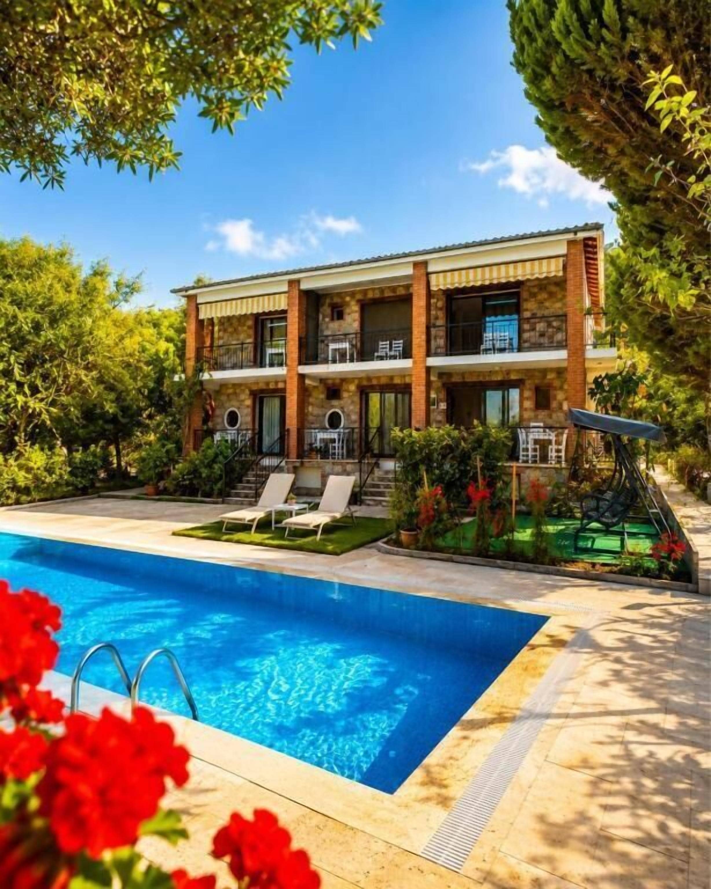 Un edificio de dos plantas con piscina, zona de estar al aire libre y abundante vegetación.