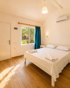 A bedroom with a bed, a window with curtains, an air conditioning unit, and a door. - Doğa pansiyon (muğla)