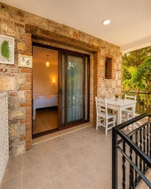 A balcony with a stone wall, a sliding glass door, a white table, and chairs. - Doğa pansiyon (muğla)