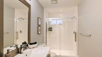 A modern bathroom with a large mirror, two sinks, a shower, and a toilet.