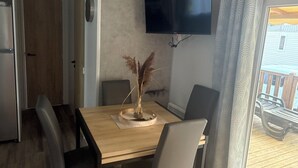 Un'area pranzo con tavolo in legno, sedie, TV a parete e vista sul terrazzo esterno.