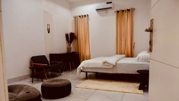A bedroom with a bed, a chair, a desk, a small ottoman, and a wall-mounted air conditioner. - Perfect 4-bedroom apartment with Starlink and 24/7 Inverter Power in Lekki (Lekki)