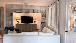 A living room with a sectional sofa, a flat-screen TV, and a bookshelf. - NEW 4BR Coastal Home with AC Steps to Kinney Shores Beach ⭐⭐⭐⭐⭐ (Saco)