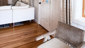 A room with a white sofa, a wicker chair, a wooden floor, a white door with a window, and a sign above the door. - NEW 4BR Coastal Home with AC Steps to Kinney Shores Beach ⭐⭐⭐⭐⭐ (Saco)