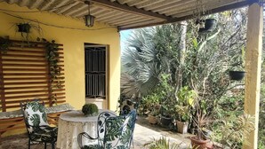 Un espacio de patio cubierto con piso de baldosas, una mesa redonda, dos sillas y varias plantas en macetas.