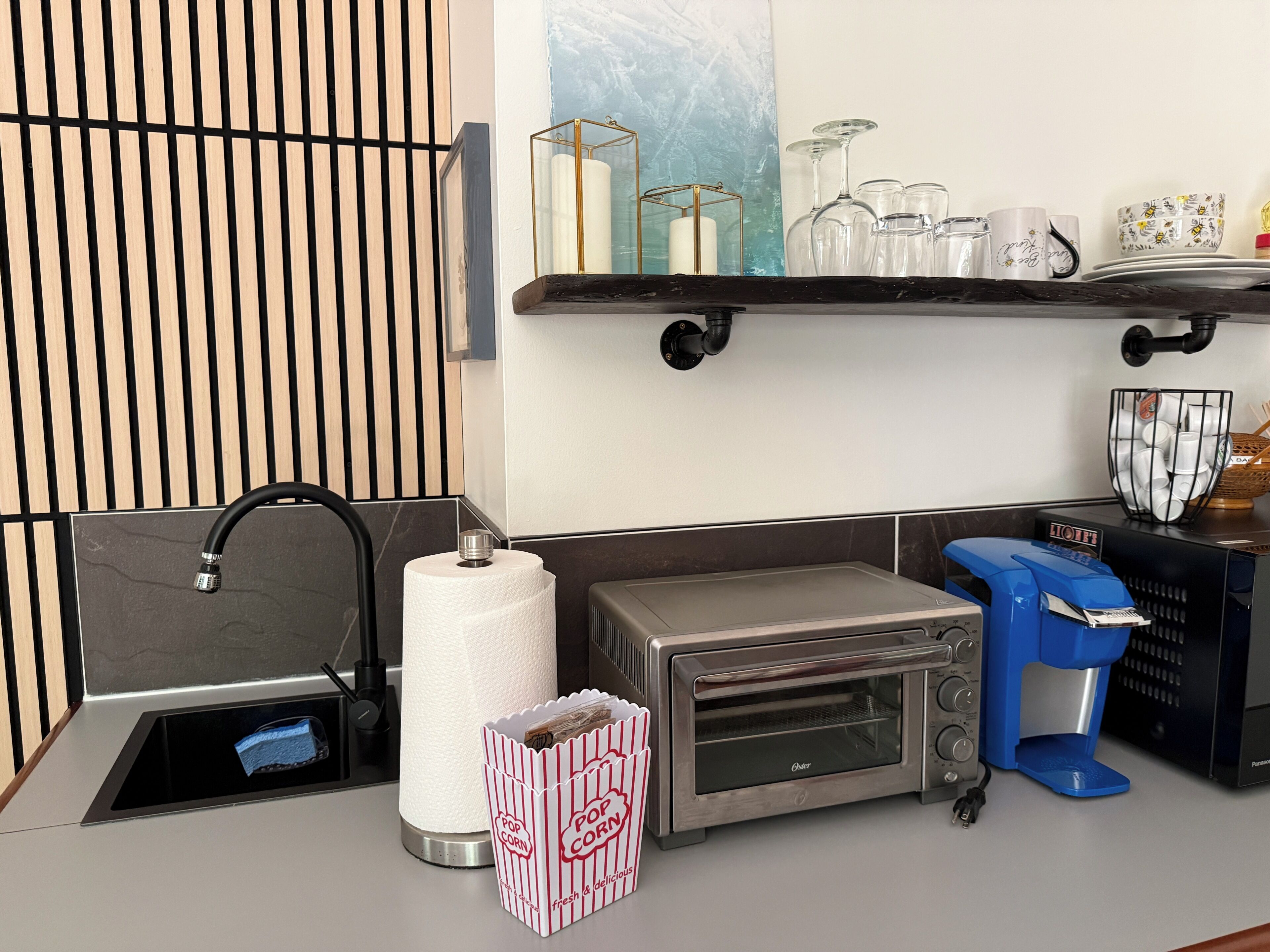 A kitchenette with a stainless steel toaster oven, a coffee maker, a paper towel dispenser, and a pop corn container.