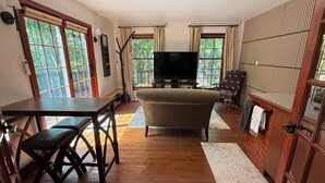 A living room with a TV, a sofa, a dining table, and a chair. - Spacious 1-bedroom suite surrounded by nature in charming Downingtown. (Downingtown)