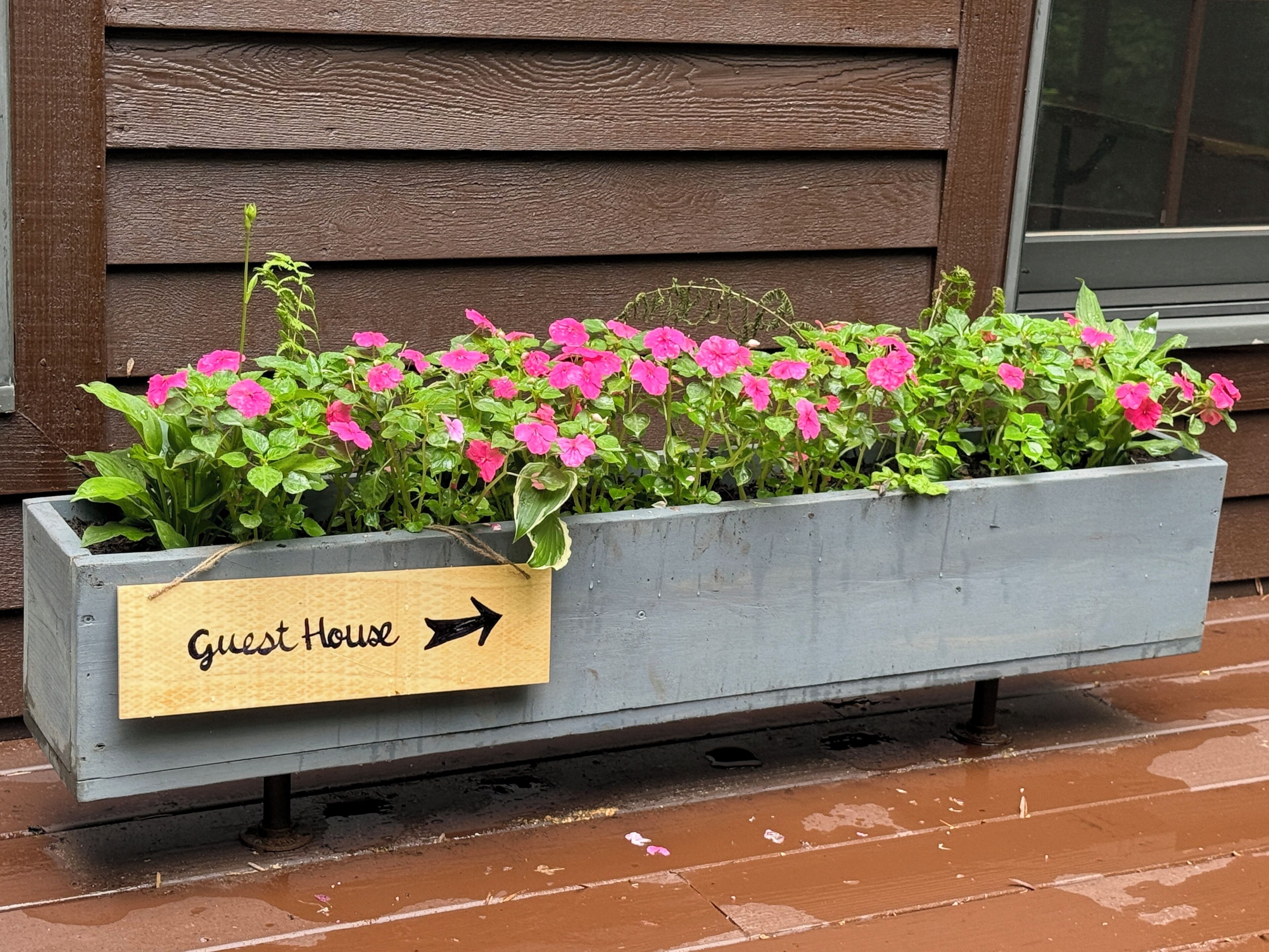 Un bac à fleurs avec une pancarte indiquant « Maison d’hôtes » et une flèche indiquant la direction.