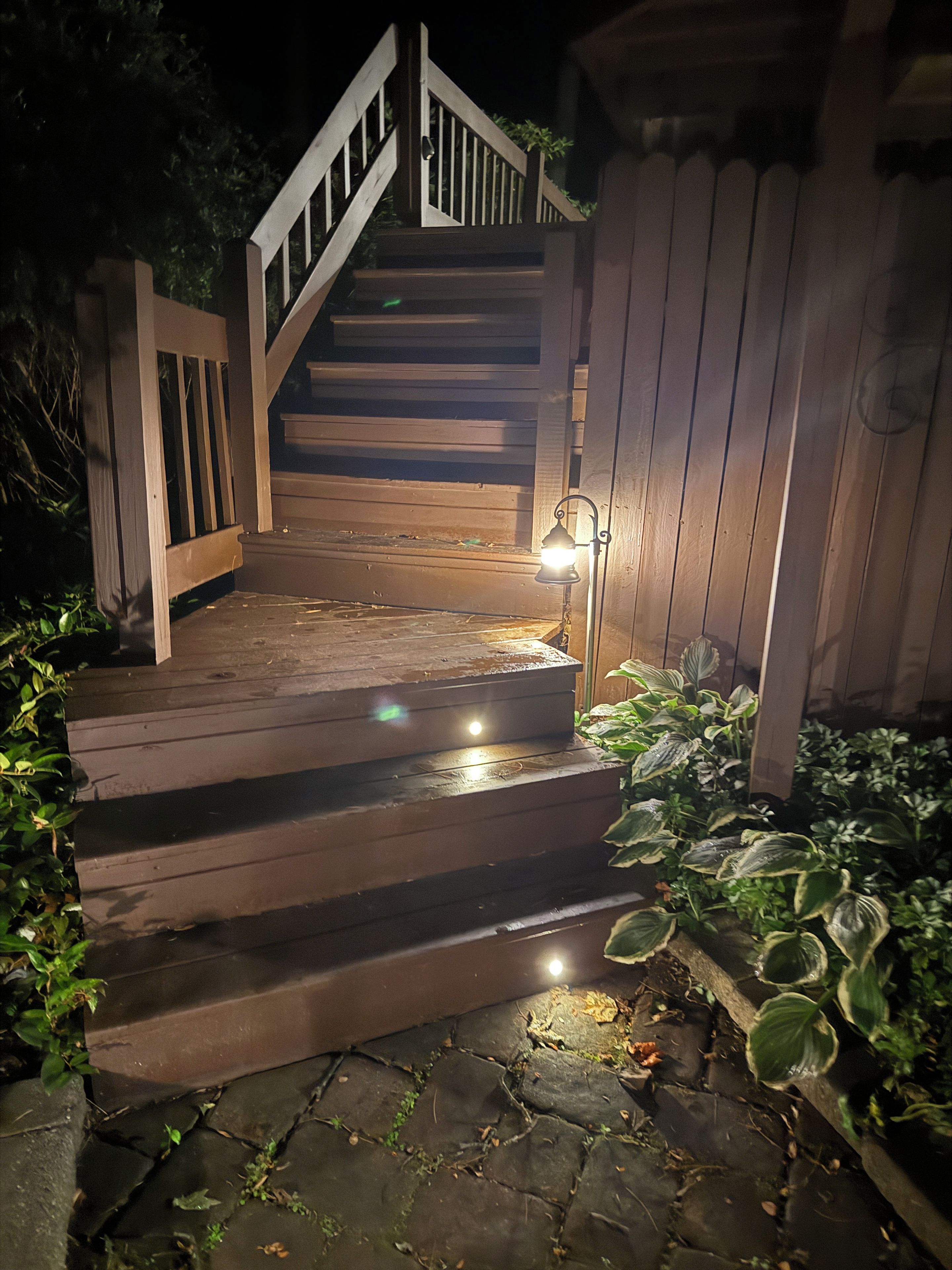Una escalera de madera que sube a una terraza con un farol al lado.