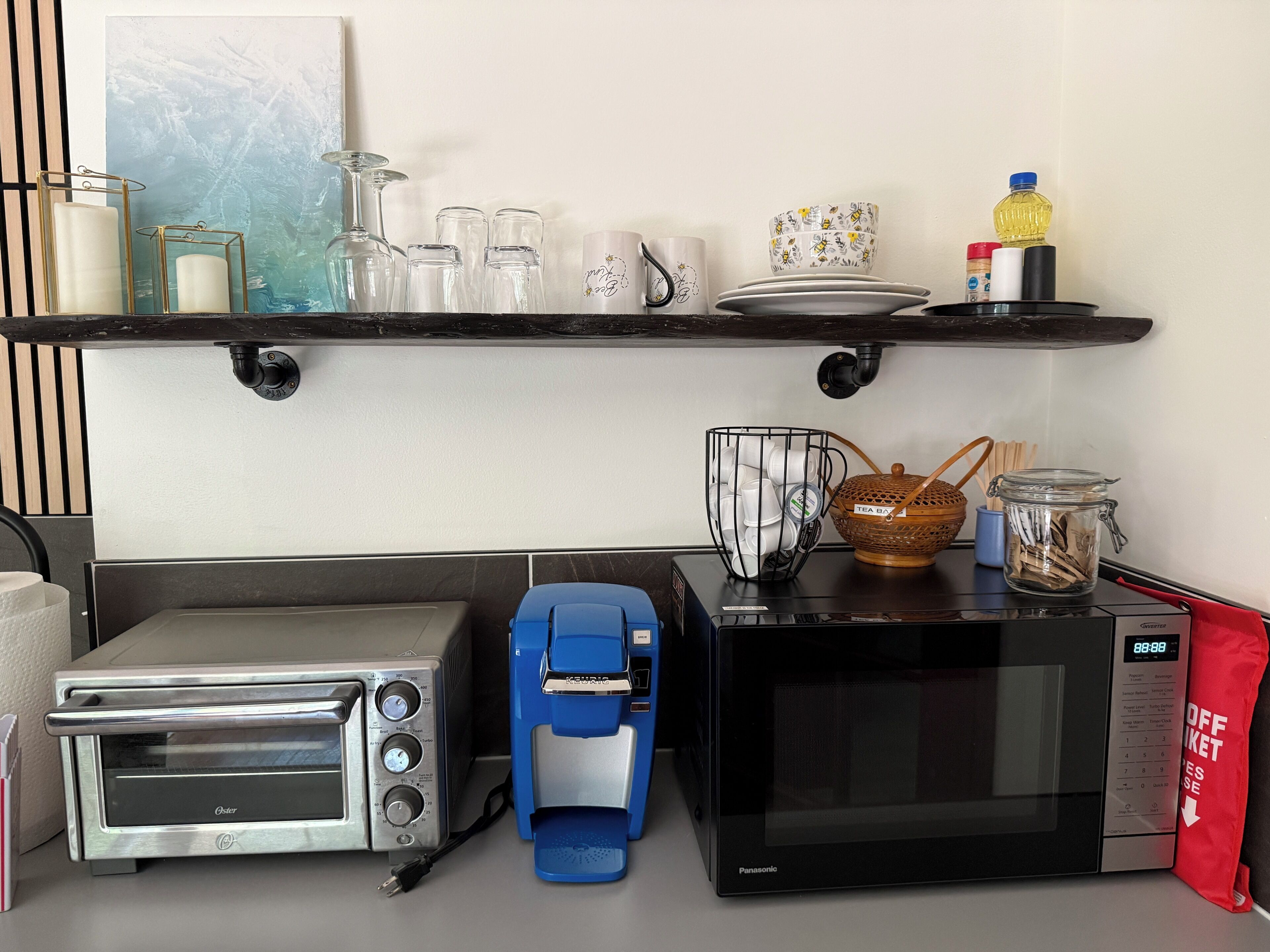 Een keuken met een broodrooster, koffiezetapparaat, magnetron en diverse keukenbenodigdheden op het aanrecht.