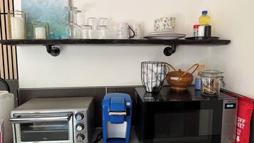 Een keuken met een broodrooster, koffiezetapparaat, magnetron en diverse keukenbenodigdheden op het aanrecht.