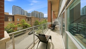A balcony with a chair, a table, and a view of high-rise buildings and trees. - Downtown Loft-style Condo | Pool, Gym & Balcony (Toronto)