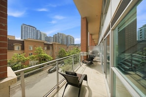 A balcony with a chair, a table, and a view of high-rise buildings and trees.