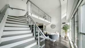 A modern interior with a staircase, a living area with a sofa, a coffee table, and a large window. - Downtown Loft-style Condo | Pool, Gym & Balcony (Toronto)