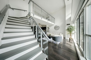 A modern interior with a staircase, a living area with a sofa, a coffee table, and a large window.