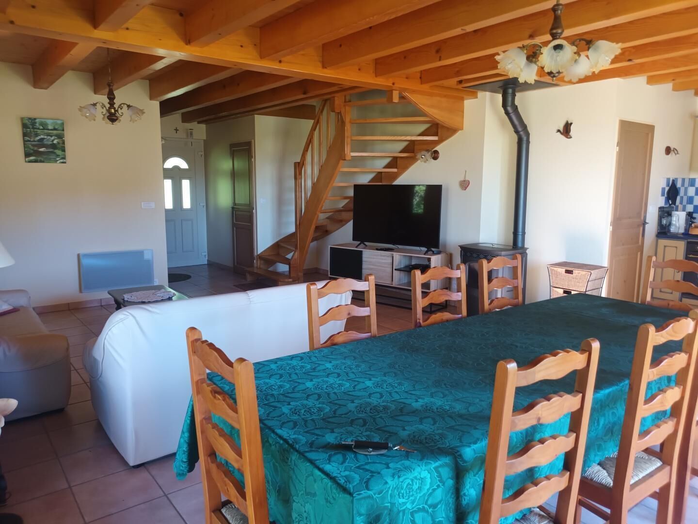 Ein gemütliches Wohnzimmer mit einer Holztreppe, einem Fernseher, einem Esstisch mit Stühlen und einem Sofa.