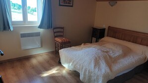 Une chambre à coucher comprenant un lit, une chaise, une table de chevet, une fenêtre avec des rideaux et un radiateur fixé au mur.